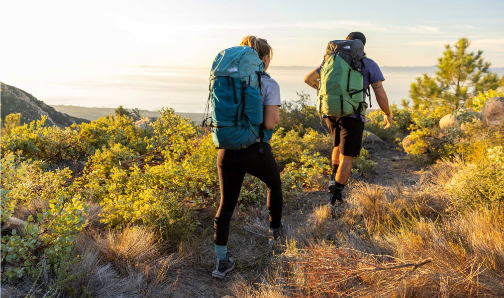 two hikers wearing north face backpacking backpacks hike along a trail