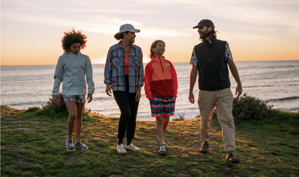 a family of four including an adult woman, adult man, a young girl and young boy are wearing TNF gear as they walk to the campsite