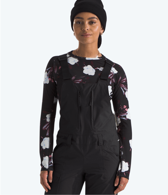 A women wearing snow bibs from The North Face standing in front of a grey background.