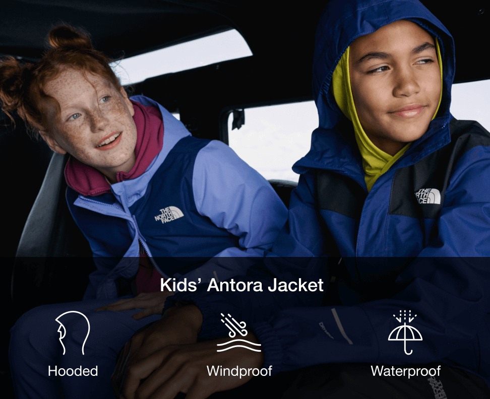 Two kids inside a car. To the left a red-headed girl in a light purple rain jacket. To the right a boy in a two-toned blue rain jacket. 