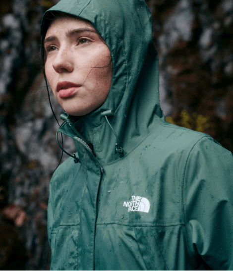 A woman in a green rain jacket with the hood up looking to the left.