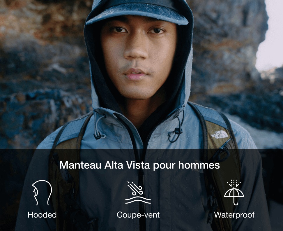 A man looking straight at the camera wearing a baseball hat with a rain hood on top of it.