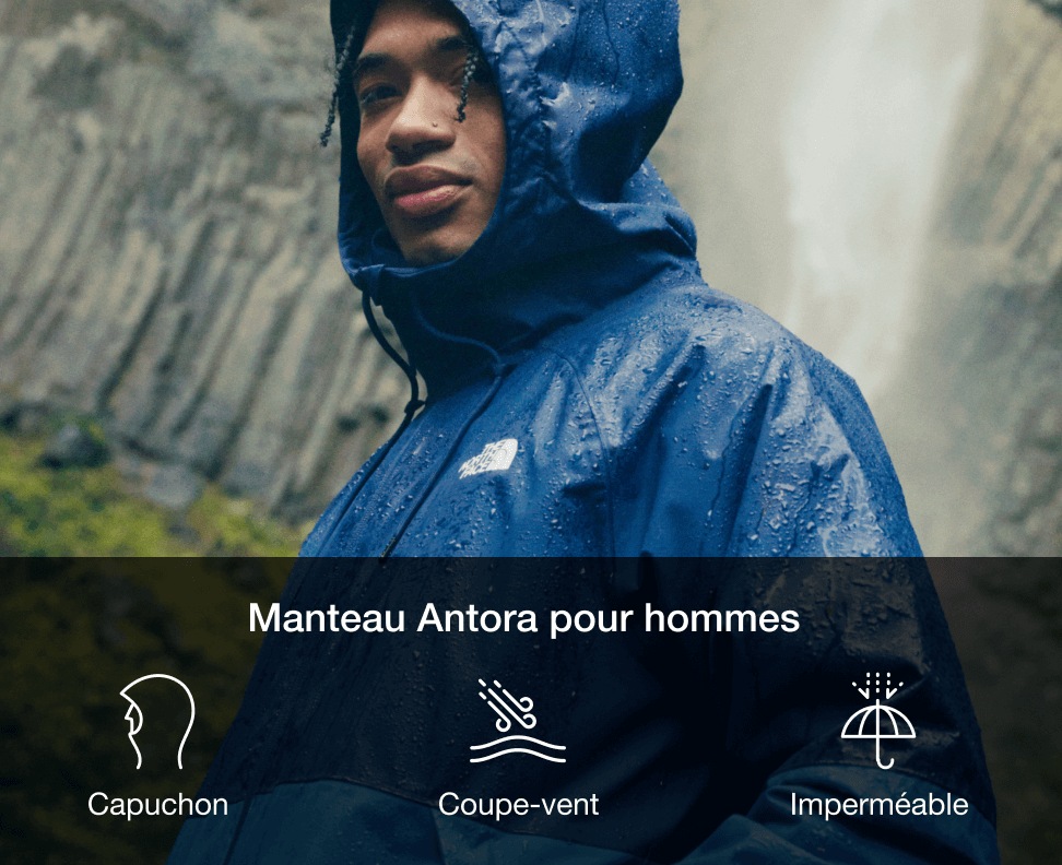 A man in a two-toned blue rain jacket with the hood up and waterfall behind him. 