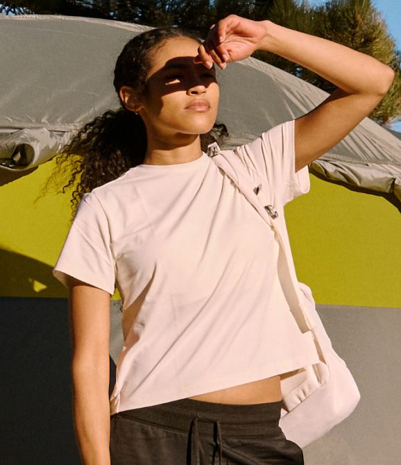 A woman wearing a white t-shirt from The North Face, standing in the sunshine.