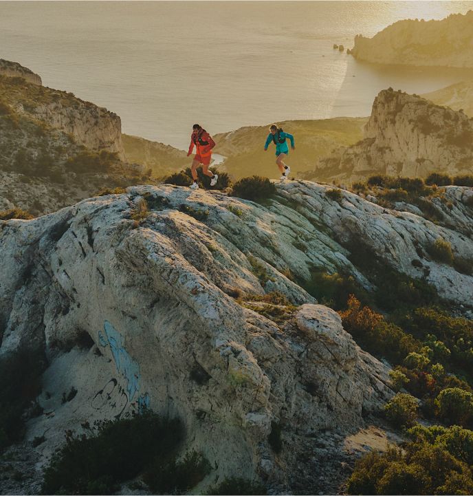 A group of four runners running uphill in soft lighting. The woman leading the way is in a blue jacket, black running shorts and purple/pink lensed sunglasses.