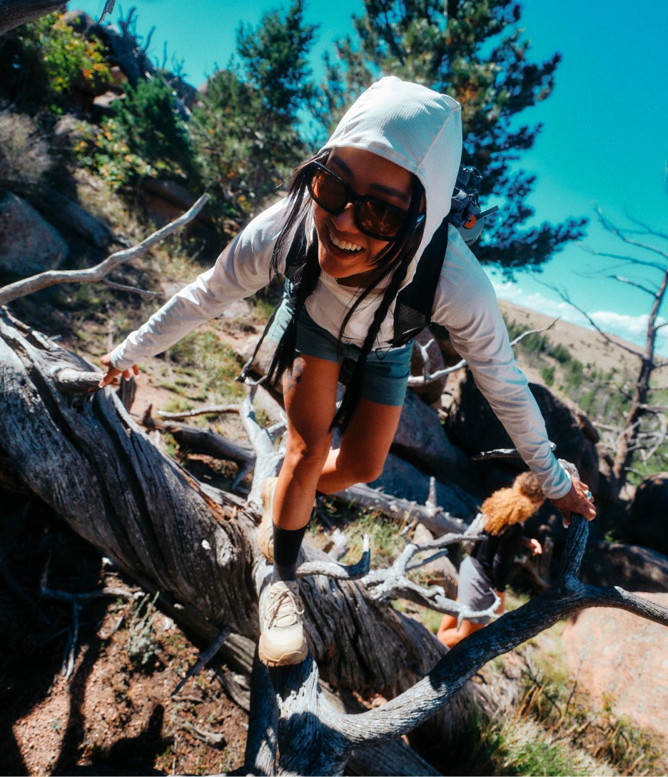 A woman in a white hoodie and sunglasses climbing over a log.