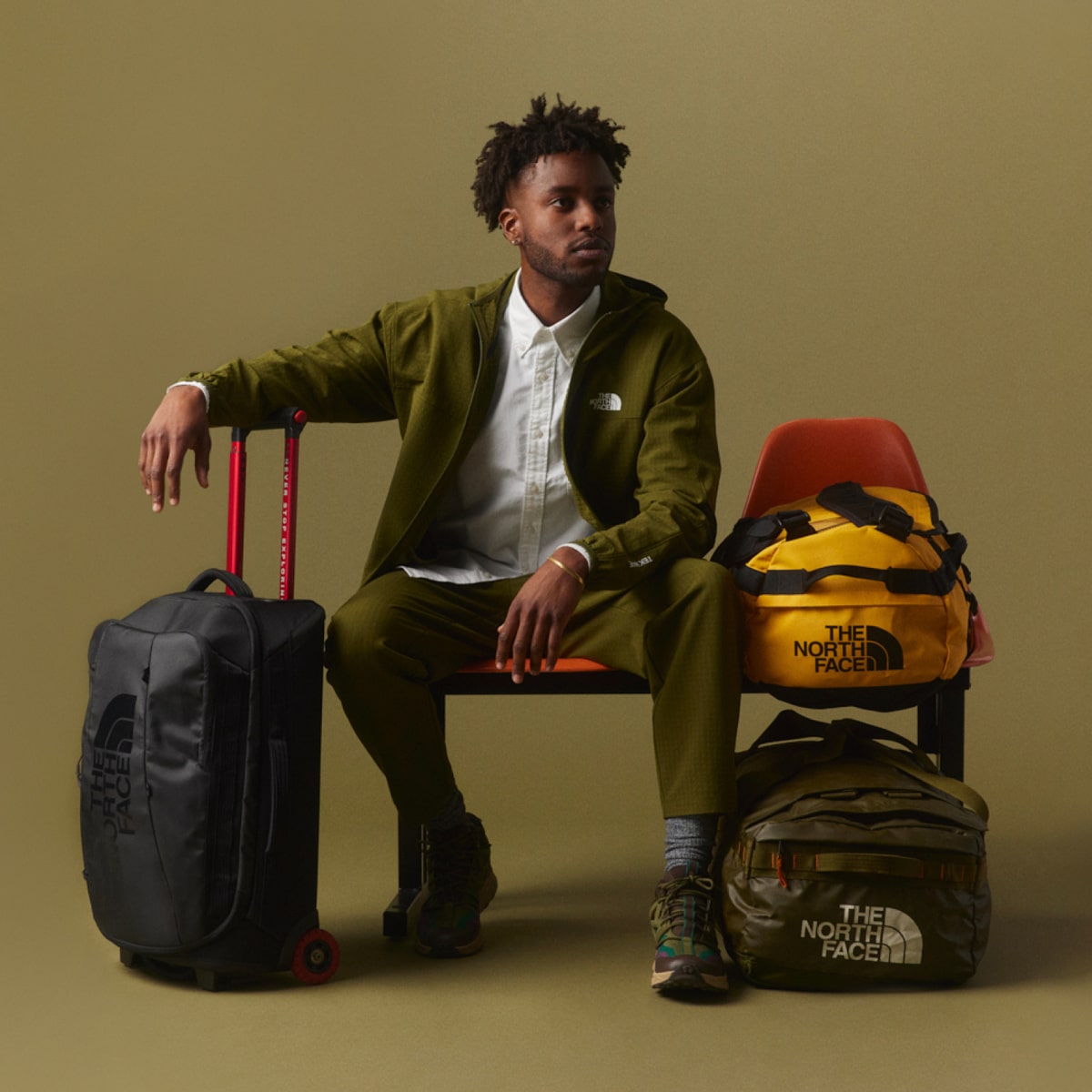 A studio image of a traveler sitting next to their fully packed luggage. 
