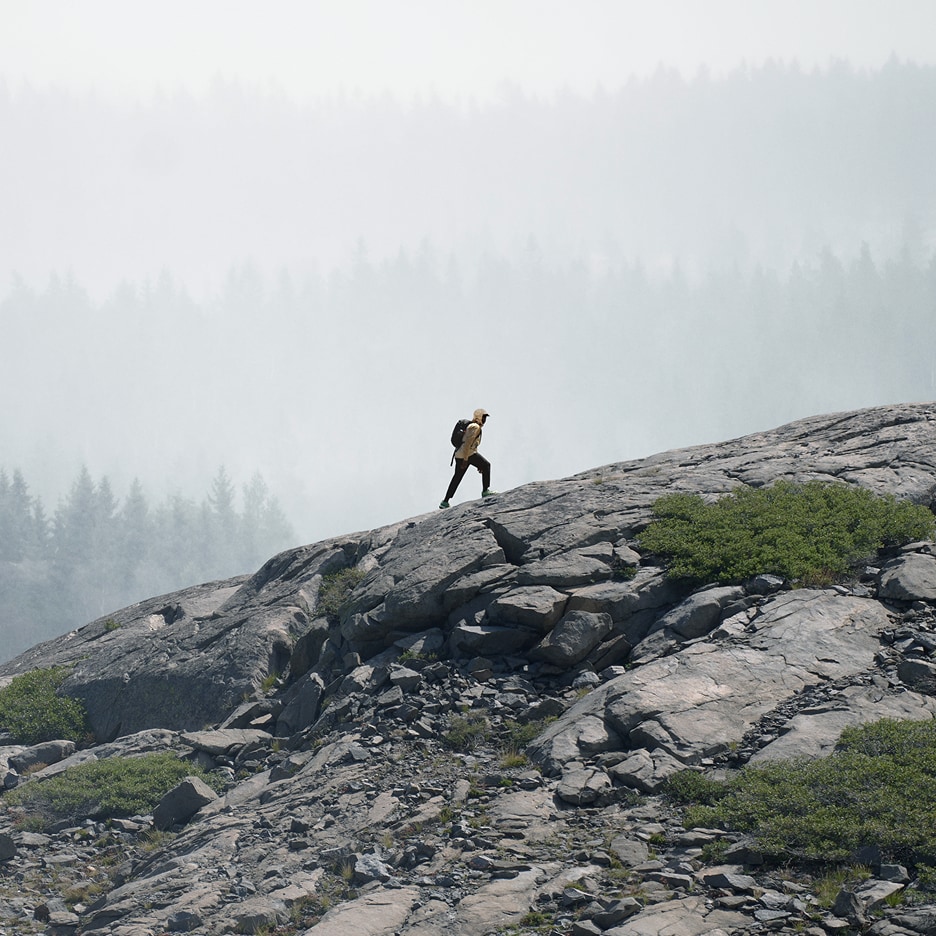 A person in a rain jacket from The North Face hikes up a rocky ridge. In the background, gray mist covers the trees.