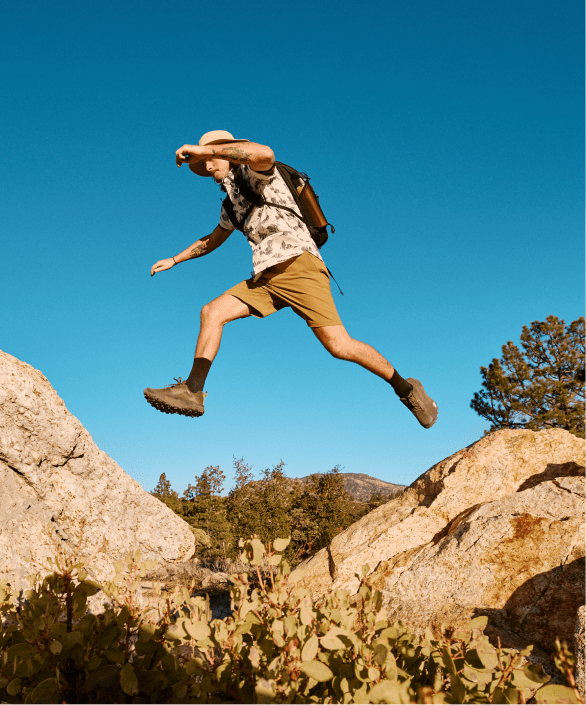 A man jumps over a ridge wearing hike apparel from The North Face.