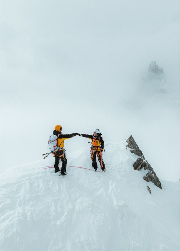 Image of two climber from The North Face fist bumping with mountain peaks in the background.
