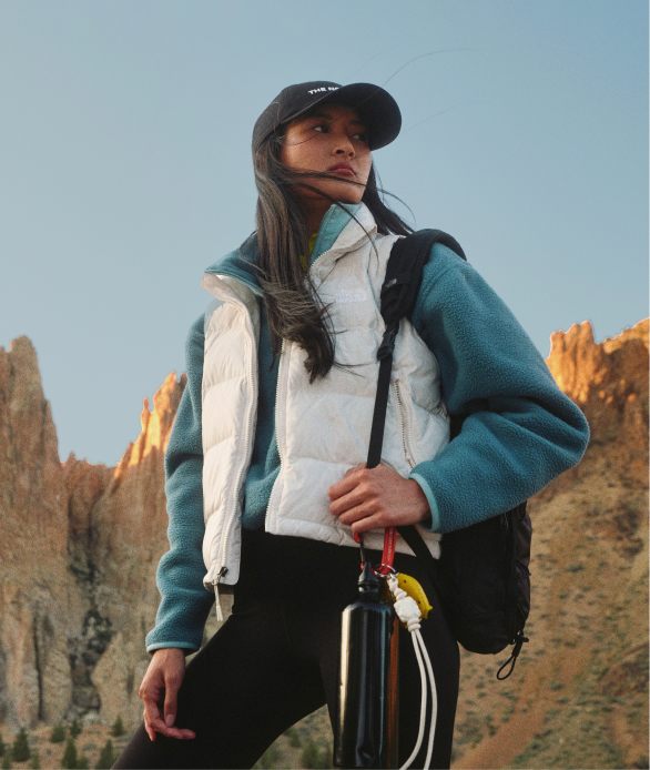 A woman in black pants and white/gray jacket, climbing a ladder.