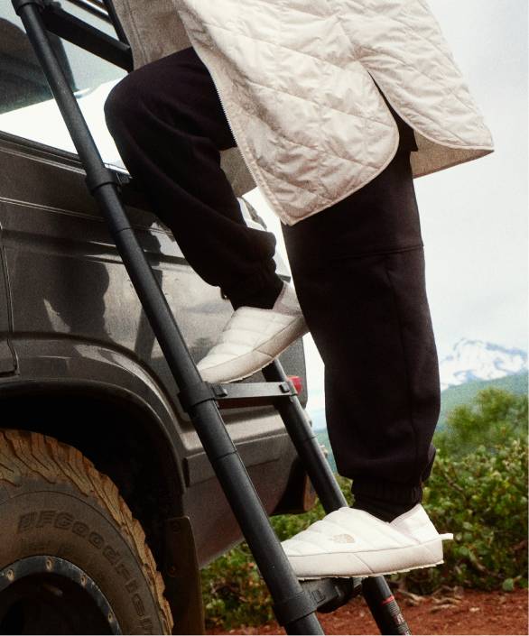 A woman in black pants and white/gray jacket, climbing a ladder.