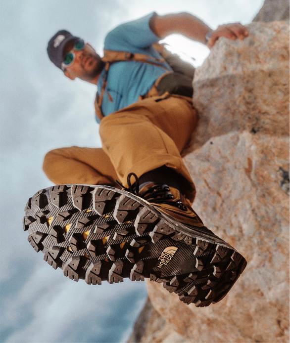 A man in a hat and sunglasses sitting on a rock with the tread of his boot in focus.