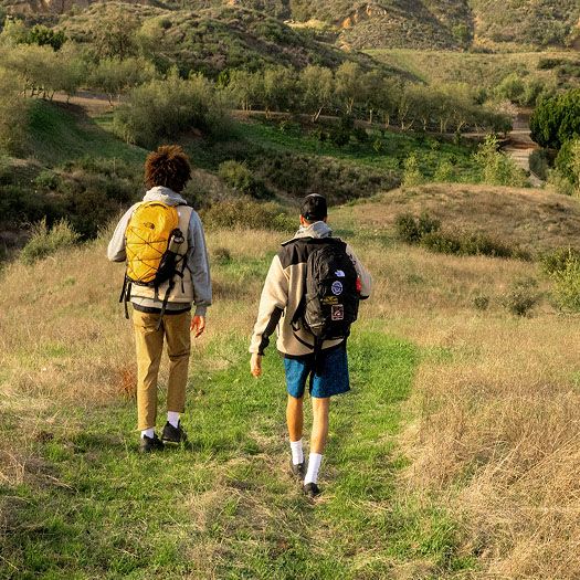 Two men hike on a grassy trail with The North Face backpacks.  