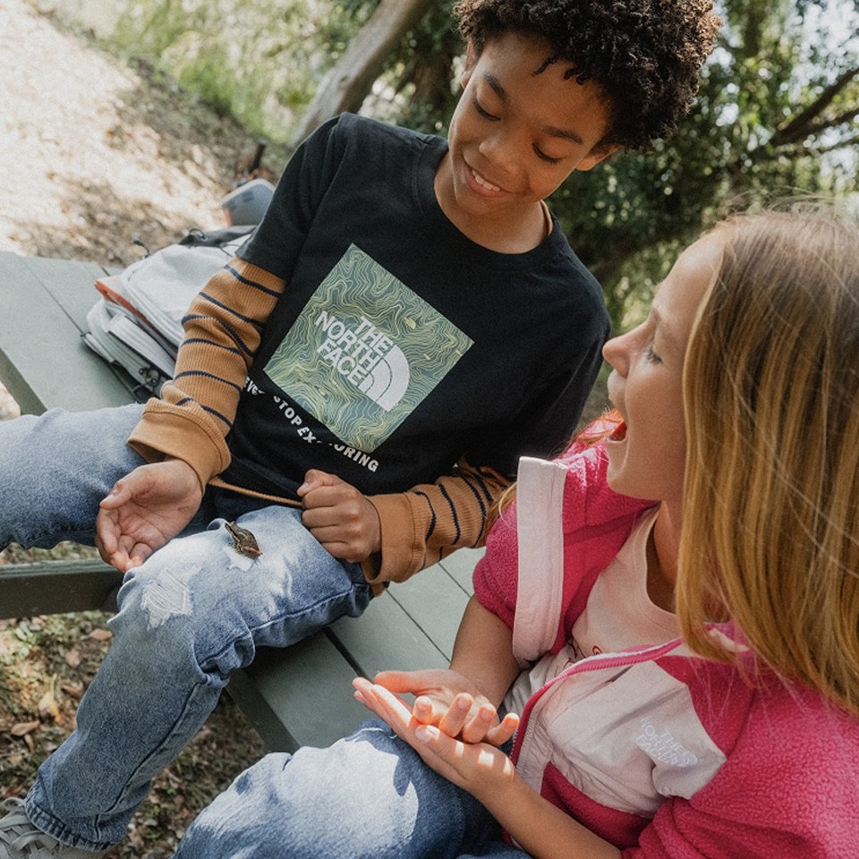 A boy and a girl sitting on a picnic table in the woods