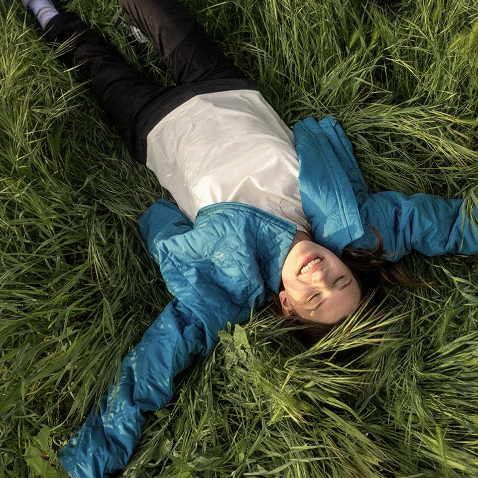 girl laying in the grass with her arms spread out in a The North Face puffer jacket