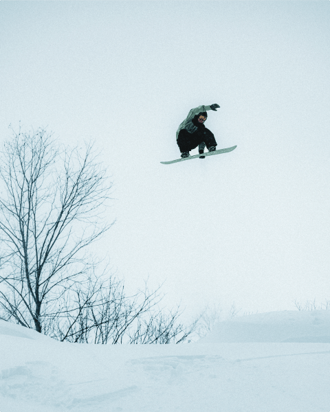 A snowboarder catching air and grabbing their board.