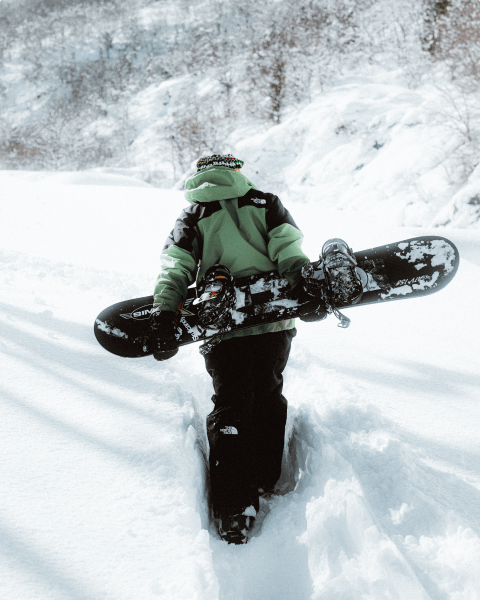 Image of a person wearing The North Face hiking up a snow covered mountain while carrying a snowboard.