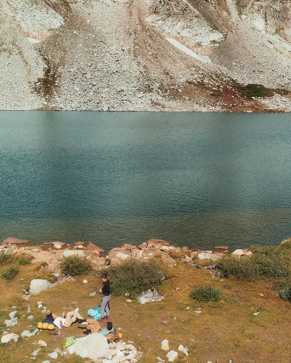High-mountain lake with hills in the background, people hanging out at the shore in the foreground.
