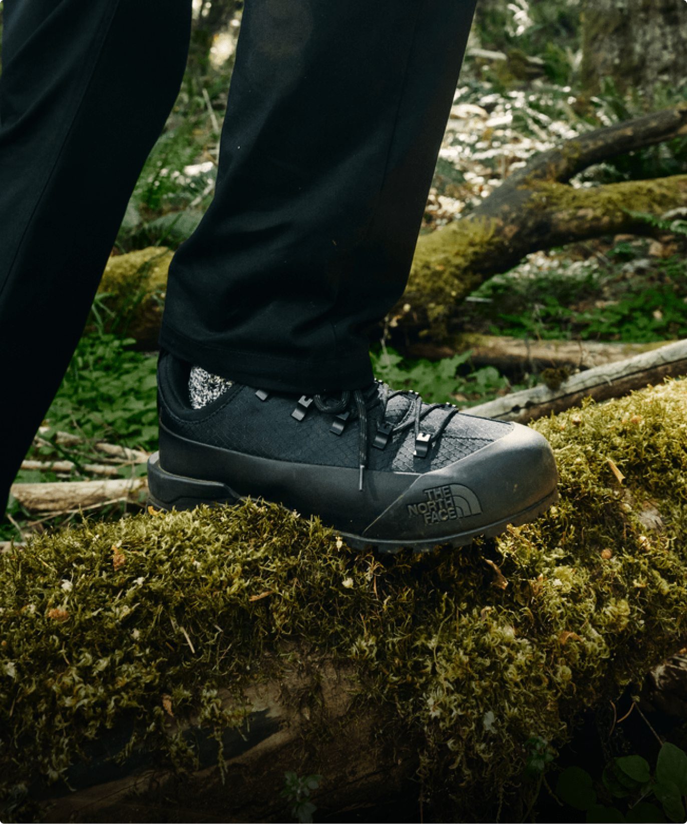 Closeup of a black TNF shoe walking in a mossy forest