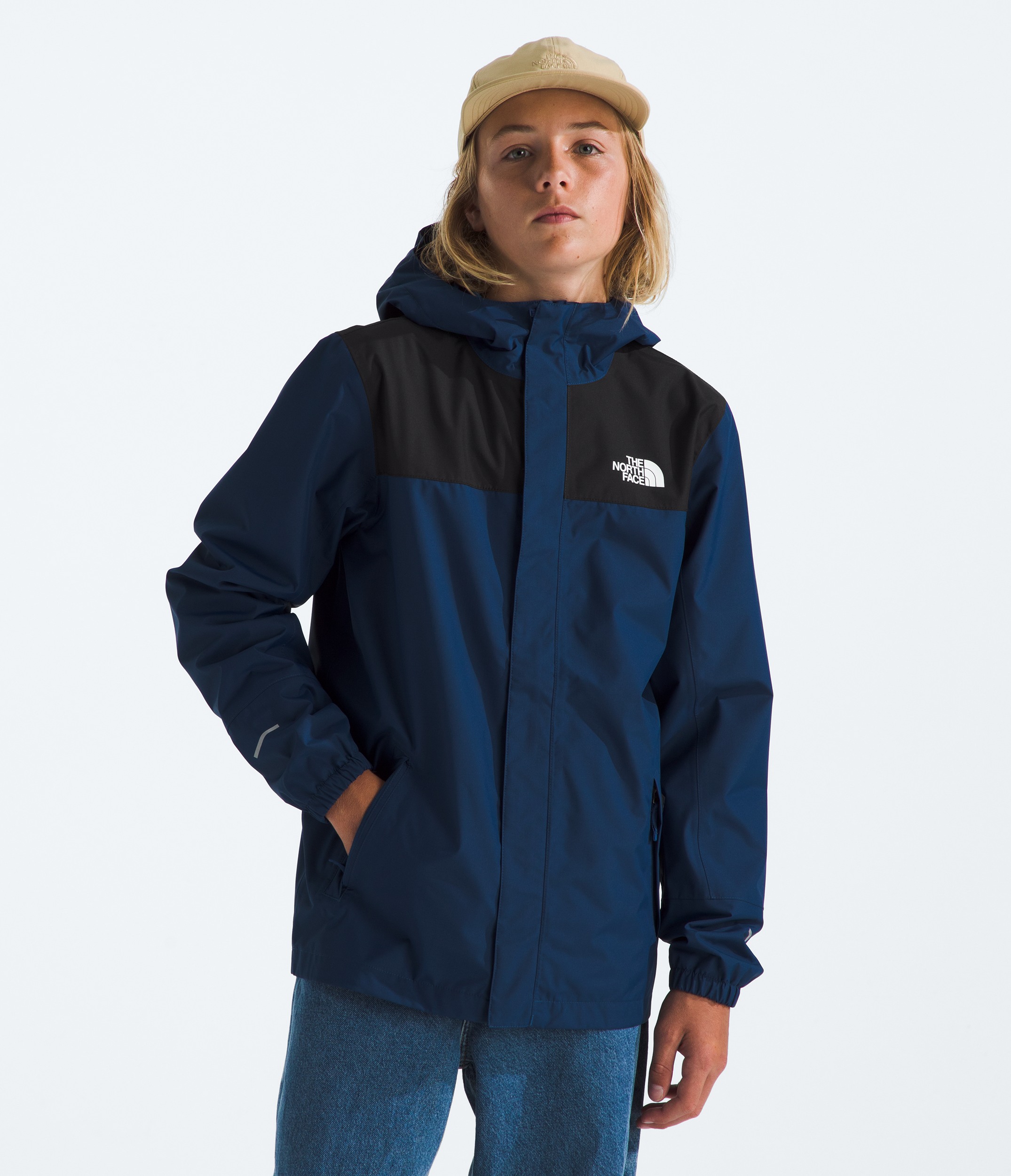 The backside of a kid in a two-toned blue rain jacket climbing down rocks to a rocky beach. 