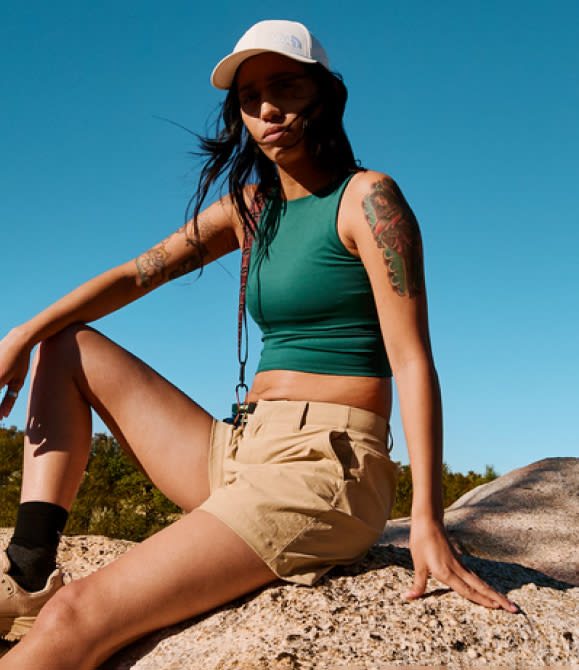 A woman sitting on a rock wearing a green tank top and khaki shorts from The North Face.