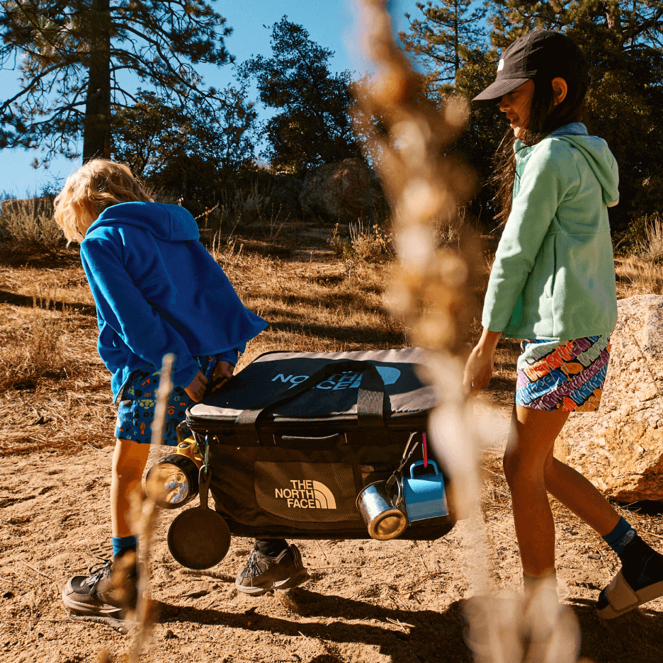 Two young campers carrying a gear box to their campsite.